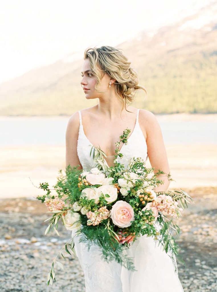 Bride with floral bouquet alongside Eklutna lake