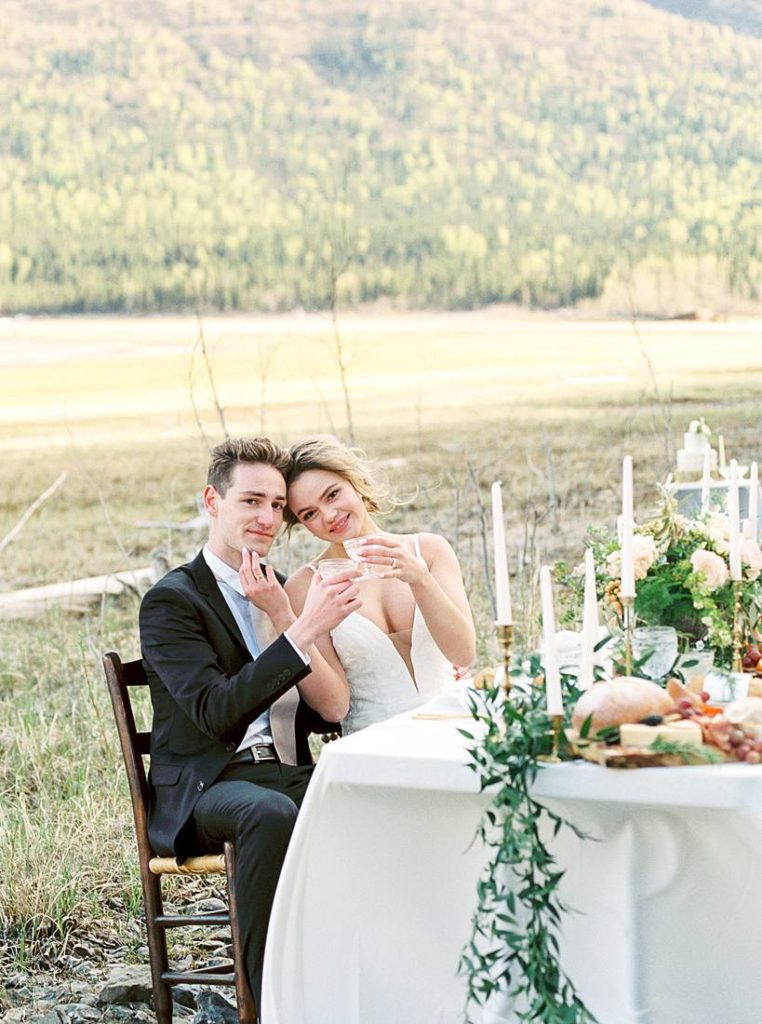 Bride and groom at Alaska destination wedding table toasting their wedding in the beautiful Alaska outdoors of Eklutna Lake